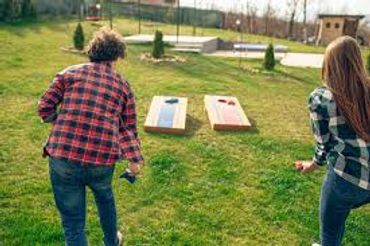 Two people playing cornhole outdoors on a grassy lawn.