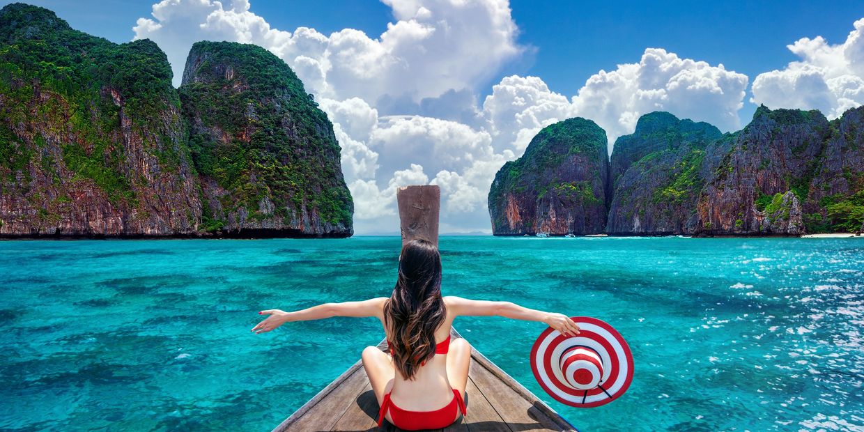 Woman in red bikini sitting on a boat amid turquoise waters and limestone cliffs.