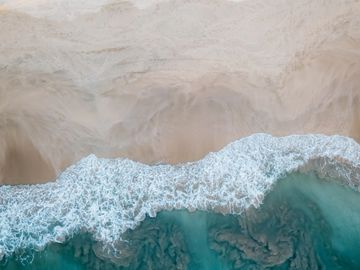 Aerial view of teal wave moving onto sand