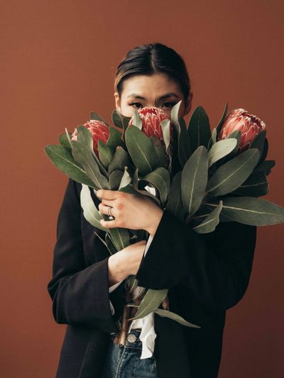 Asian woman staring at camera hidden behind flowers with brown background