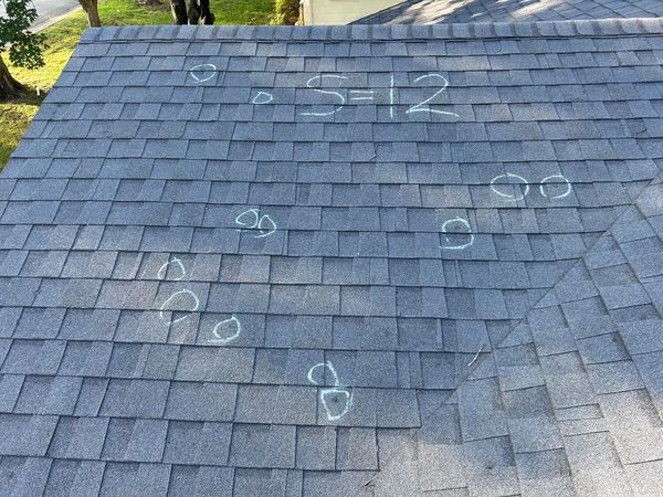 Chalk markings on a shingled roof indicating damage spots.