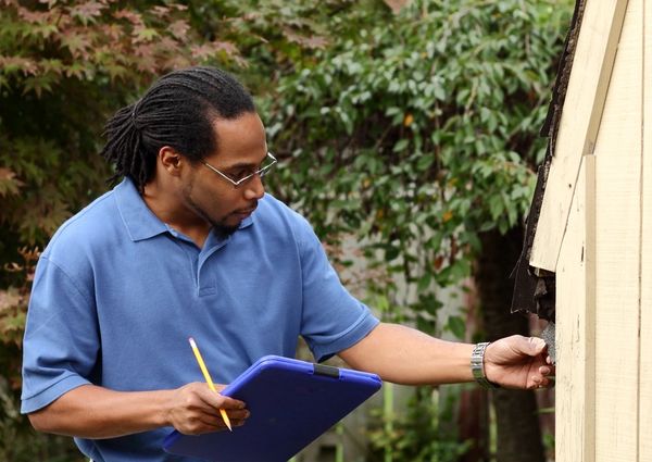 Man inspecting a wooden structure with clipboard and pencil.