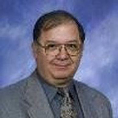 Middle-aged man in glasses and suit against a blue backdrop.