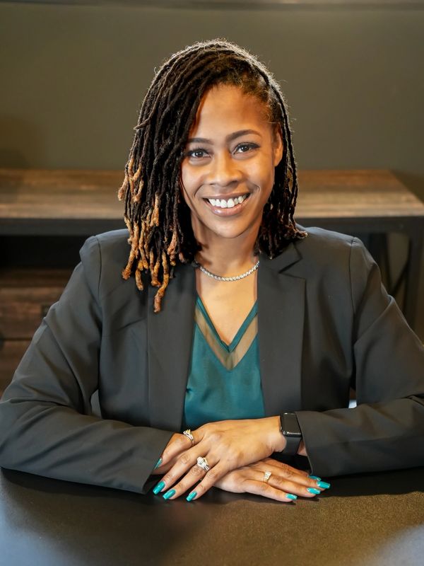 Smiling woman with dreadlocks in a black blazer.