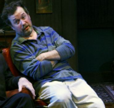 Man sitting in a chair with arms crossed, wearing a striped shirt.