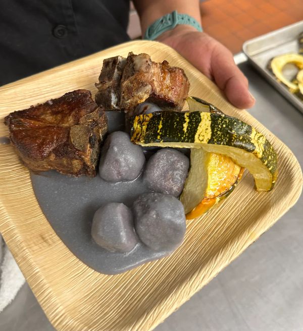 Plate with roasted meat, squash, and purple gnocchi in sauce.