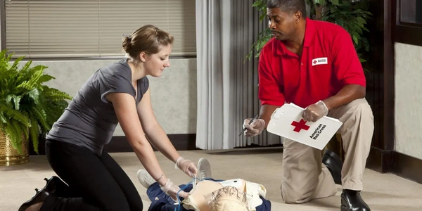 Two people practicing CPR on a medical dummy indoors.