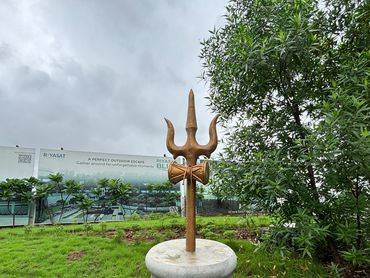 Golden trident statue on stone base in a garden.