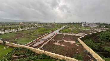 Overcast sky above a vast green development area with roads and plots.