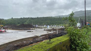 Construction site with cloudy sky and green hills in the background.