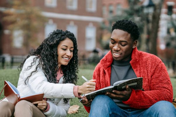 Two students studying together outdoors, sharing a notebook. We offer a student discount. We offer print services for all of treasure valley, including Boise, Meridian, Nampa, Kuna, Eagle, Caldwell, Middleton, Melba, Marsing, Star, Emmett, and Horseshoe Bend.