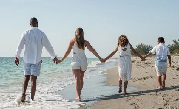 Family walking hand in hand along the beach shore.