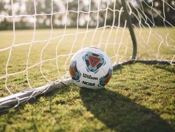 Wilson NCAA soccer ball near goal net on grass.