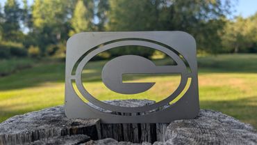 Metal Green Bay Packers logo on a tree stump outdoors.