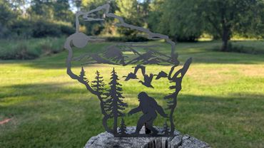 Metal art of Wisconsin with Bigfoot, trees, mountains, and flying geese.