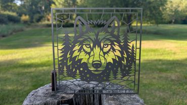 Metal wolf art piece with forest design on wood stump.