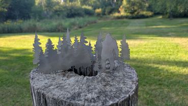 Metal art of a forest and Bigfoot on a tree stump outdoors.