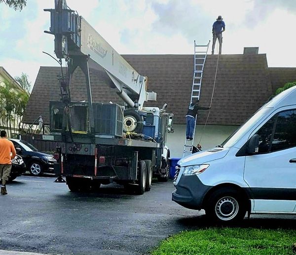 Workers use a ladder and rope to climb a steep roof with a crane truck nearby.