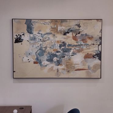 Abstract painting with neutral and blue tones hanging on a beige wall.