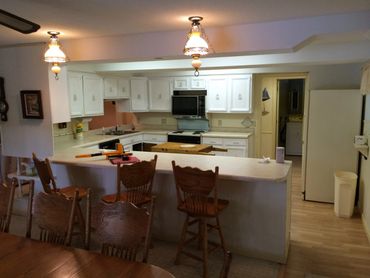 A clean kitchen with white cabinets brown chairs
