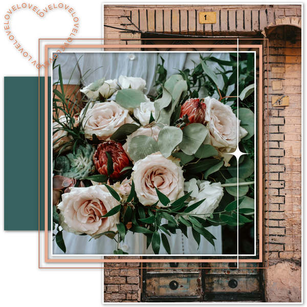 A bouquet of pink and white roses with palm and eucalyptus leaves sits in front of a terracotta wall