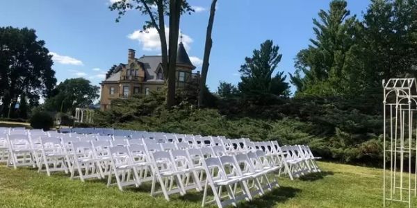 Outdoor wedding setup with rows of white chairs.