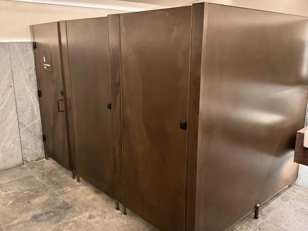 A row of brown restroom stalls with bronze liquid metal doors in a public bathroom.