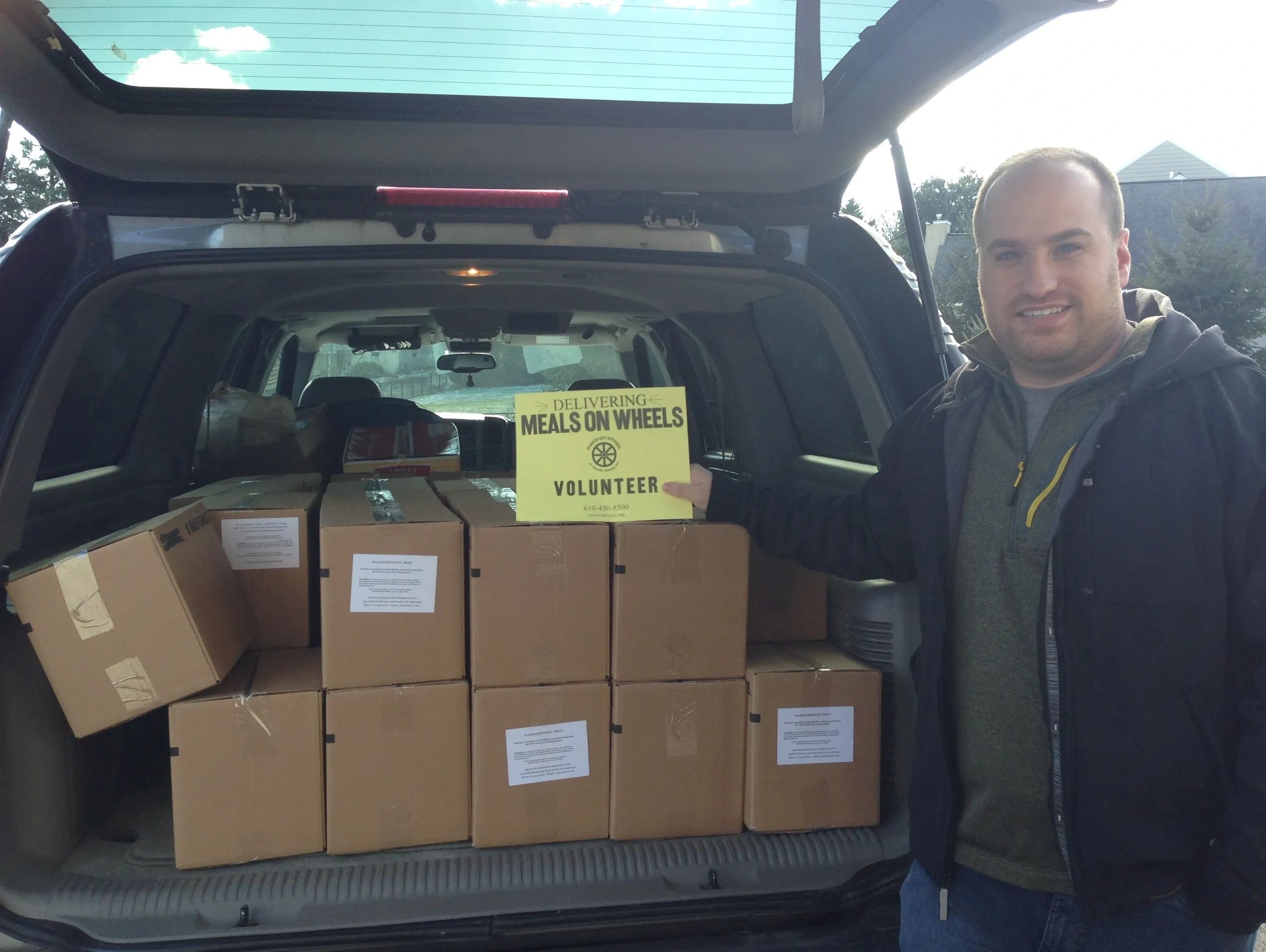 Man prepares to deliver Meals on Wheels with boxes in car trunk.
