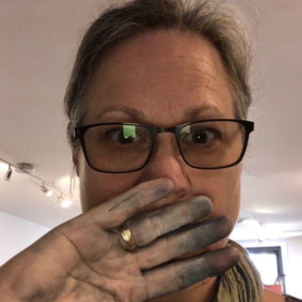 Woman with glasses and dirty hands covering her mouth indoors.