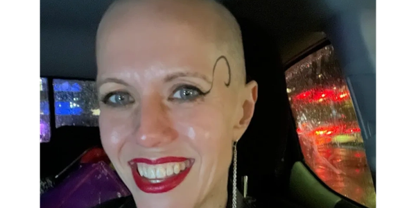 Smiling person with bold makeup and a unique ear accessory in a car at night.