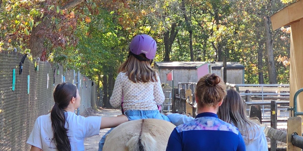 Client on a horse, working with a speech therapy treatment team moving forward on an outdoor path