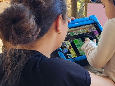 Child using an AAC system on a horse in a speech therapy session.