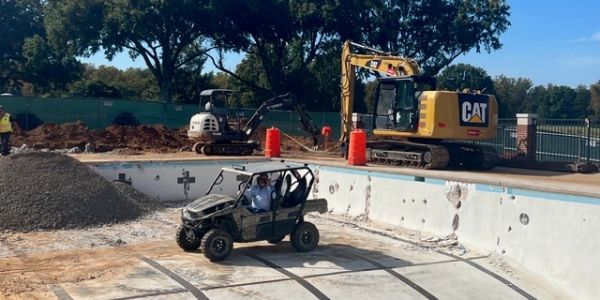 Construction inside an empty swimming pool with vehicles and workers.