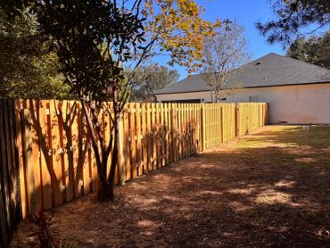 New wooden fence with trees and a house in the background.