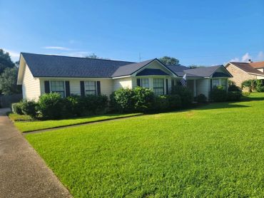Single-story house with dark roof and green lawn.