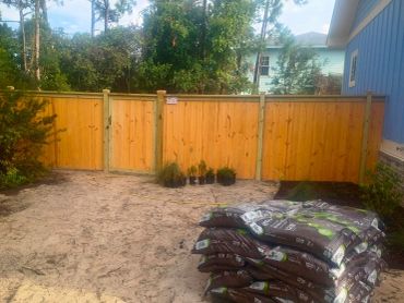 New wooden fence with bags of mulch and plants nearby.
