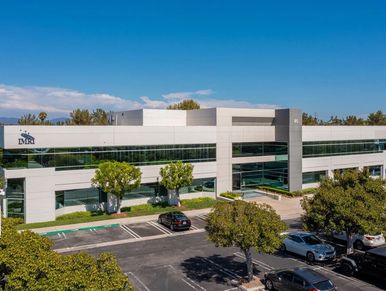Modern office building with large windows and parking lot under clear blue sky.