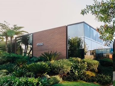 Modern commercial building with reflective glass and lush greenery.