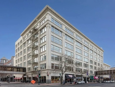 Large historic commercial building with multiple windows and skywalks on a city street corner.