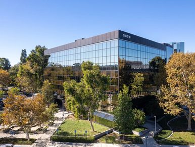 Modern office building with reflective glass windows surrounded by trees.