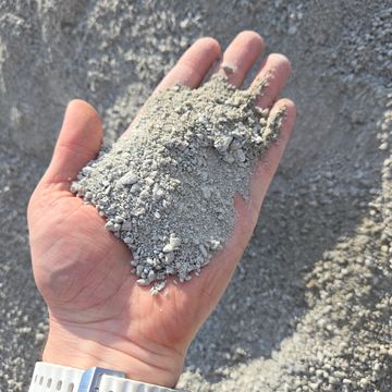 Hand holding a handful of gray gravel or crushed stone.