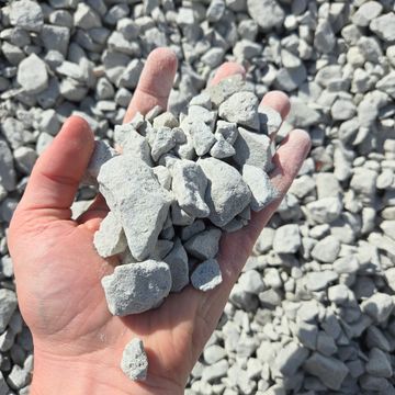 A hand holding a handful of small gray rocks outdoors.