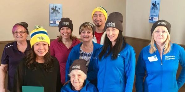 Group of smiling people wearing 'coldest night' hats.