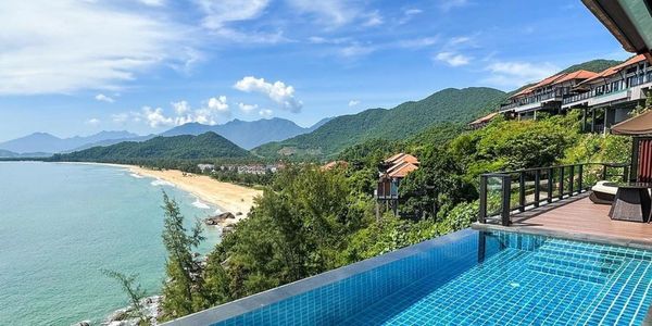 Infinity pool overlooking a scenic beach and mountains on a clear day.