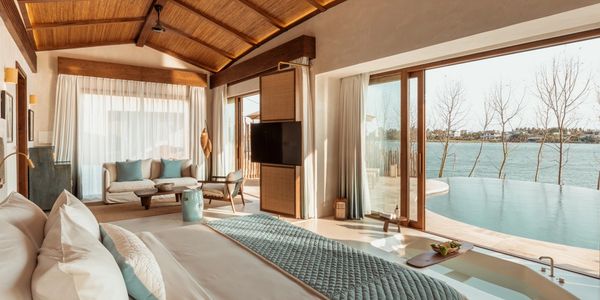 Luxurious bedroom with a large bed, sitting area, and stunning water view through glass doors.