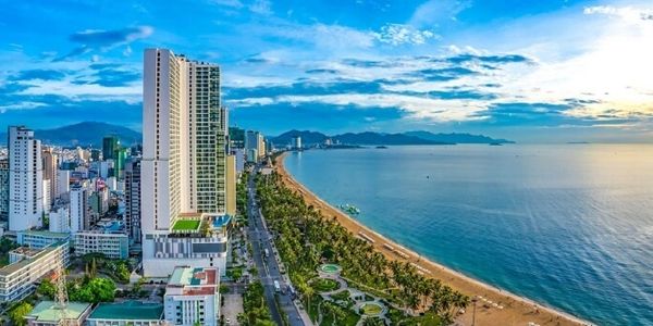 Coastal cityscape with high-rise buildings and a sandy beach under a blue sky.