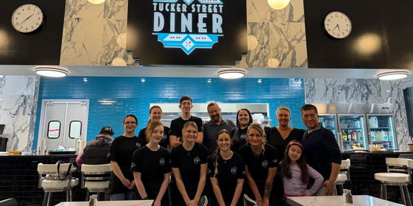 Tucker Street Diner team posing inside their stylish diner with a blue and marble backdrop.