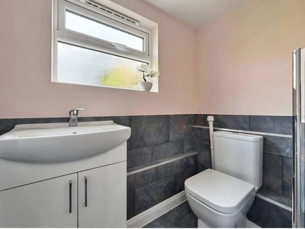 Modern bathroom with white sink and toilet, gray tiled walls, and small window with plant.