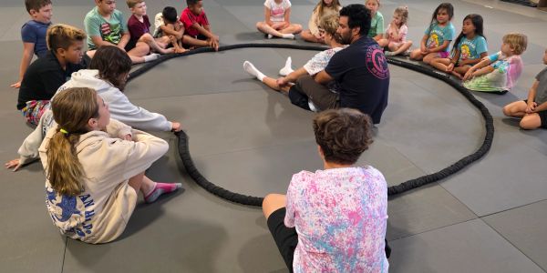 Children and an adult sitting in a circle on a mat.