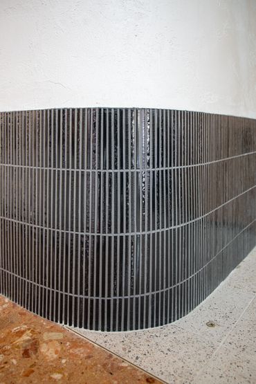 Feature curved wall with white render and black tiles.